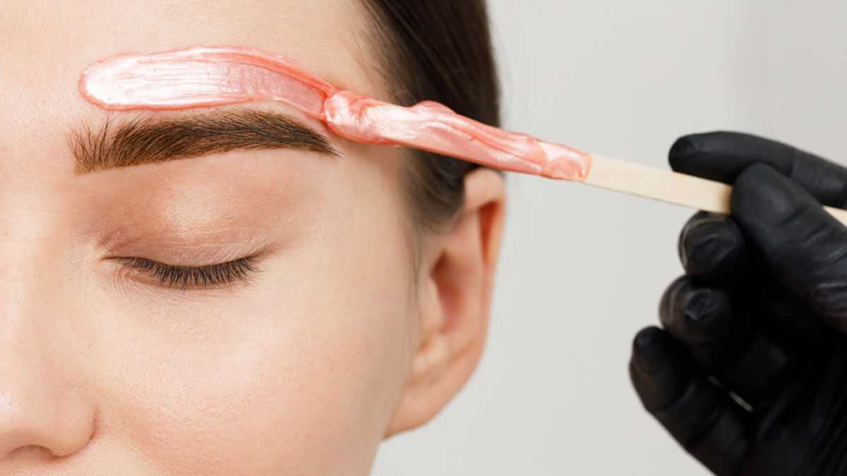 Person receiving wax treatment on eyebrow with applicator stick.